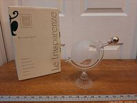 Decanter on stand with stopper beside branded box