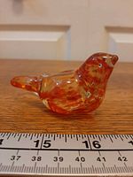 Side view of mottled red/orange glass bird next to ruler showing length