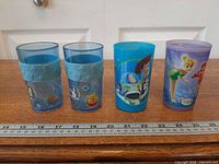 Front view of four Disney tumblers showing character graphics and ruler for scale