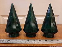 Front view of three identical green ribbed glass trees with ruler for scale