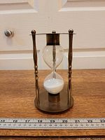 Full frontal view showing brass frame, glass bulbs, white sand, ruler indicates size