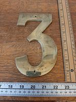 Front view of brass number 3 with rulers showing size