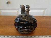 Front view of glazed ceramic walnut dish with squirrel lid beside ruler for scale