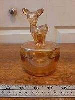 Full view of covered dish with fawn handle beside ruler