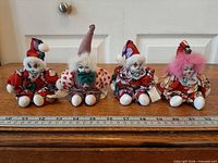 Four porcelain clown dolls in a row with ruler for scale