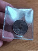 Coin front in plastic sleeve showing ONE CENT 1902 and drilled hole