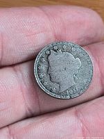 Obverse of 1911 Liberty Head nickel on fingertips, shows Liberty head silhouette and date