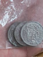 Three Canadian 50-cent coins reverse side with coat of arms visible in plastic bag