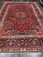 Full view of red Persian Mashhad rug on dark floor showing complete layout and borders