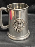 Full view of stainless steel tankard front showing emblem, handle and base