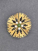 Front view showing gold-tone radial design with jade center and five pearls