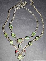 Full view of both sterling silver necklaces showing chain styles, green stones, red accents