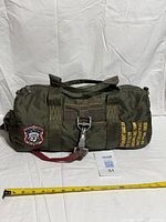 Full view of olive nylon duffel bag with tape measure for scale