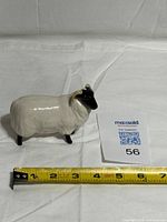 Front side view of ceramic sheep figurine next to tape measure showing length