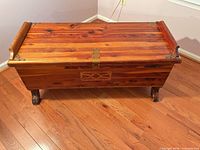 Full view of cedar chest on hardwood floor showing size, wood grain, rim ends and feet