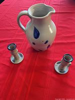 Pitcher with two candlestick holders on red tablecloth