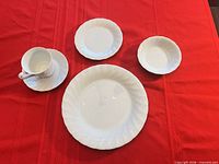 One dinner plate, one dessert plate, one bowl, one cup with saucer displayed on red cloth