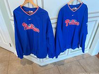 Front view of both Nike Phillies windbreakers hanging side by side showing overall condition and design