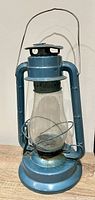 Full view of blue metal hurricane lantern showing globe, handle and base