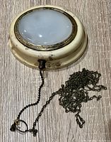 Front view showing milk glass lens, cream metal housing, brass-tone bezel, pull chain with extension