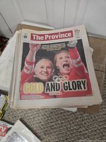 Stack of newspapers top issue headline Gold and Glory showing two Canadian athletes