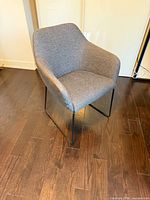 Front angled view of grey Ikea Tossberg chair on dark wood floor