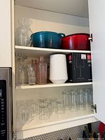 Cabinet shelf with blue and red Dutch ovens, clear glass vase, additional shelf of assorted glassware