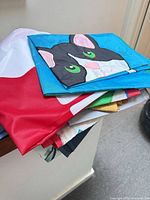 Stack of folded nylon and fabric flags, visible cat design on top, red and white flag beneath
