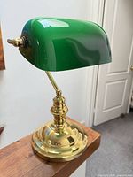 Full view of brass banker lamp with green glass shade on wooden surface