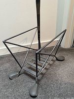 Front angle of metal magazine rack showing golf shaft handle and iron head feet