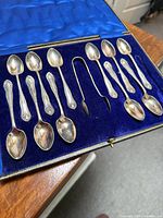 Open case showing 11 teaspoons and sugar tongs