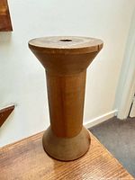 Side view of one wooden textile spool showing tapered shape and centre bore.