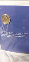 Coin on blue side of presentation card with bilingual text visible