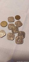 Group of square silver-tone coins and two round brass-tone coins on cloth surface