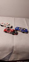 Three die-cast cars grouped on fabric background: white #3, black/red #8, blue #99