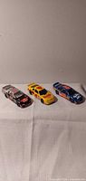 Three die-cast NASCAR cars lined up: black/silver #55, yellow #4 Kodak, blue/red model