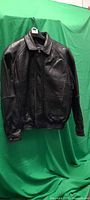 Front view of black leather jacket on hanger showing zipper, collar and elastic waistband