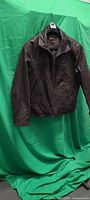 Front view of dark brown leather jacket on hanger against green backdrop