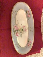 Top view of oval porcelain serving dish with rose decoration, blue border and gold rim