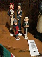 Four resin Victorian caroler figurines standing on shelf