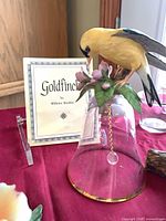 Goldfinch figurine on glass bell with identification card visible
