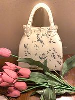 Front view of white speckled glass purse vase with faux tulips placed in front