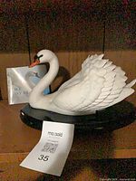 Front view of porcelain swan on black base with booklet