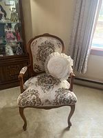 Front view of carved wood parlor chair with floral tapestry upholstery and round pillow