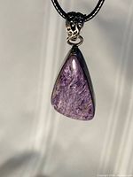 Front view of charoite pendant on black cord showing color and setting