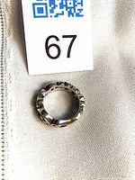 Top view of sterling silver scroll band ring beside lot tag