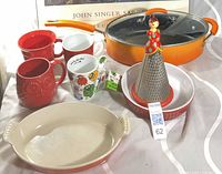 Group shot of all items—Rachael Ray pot, Le Creuset dish, red pie dish, cone grater, two red mugs, Wacky Woollies mug with spoon