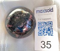 Top view of polished rhodonite palm stone beside lot card