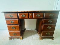 Front view of wooden desk showing all nine drawers and ornate pulls