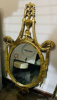 Full view of antique gold gilt oval mirror leaning against wall